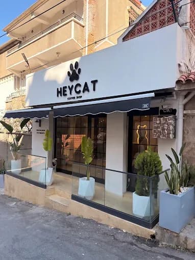 La devanture de HEYCAT Coffee Shop : un bandeau blanc avec une patte noire au-dessus du nom, un store festonné, des vitrines à cadres noirs et des bacs clairs sur le trottoir.